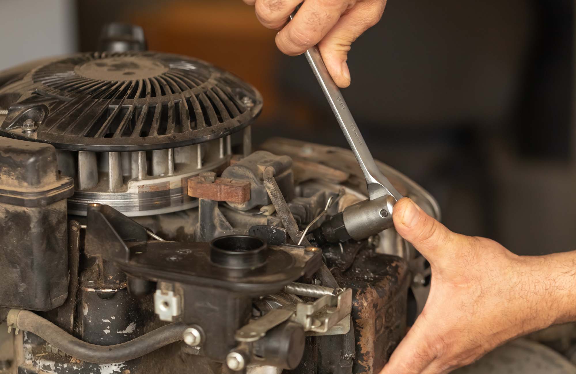 A man repairs the engine of a gasoline lawn mower. Close-up hands holding wrench