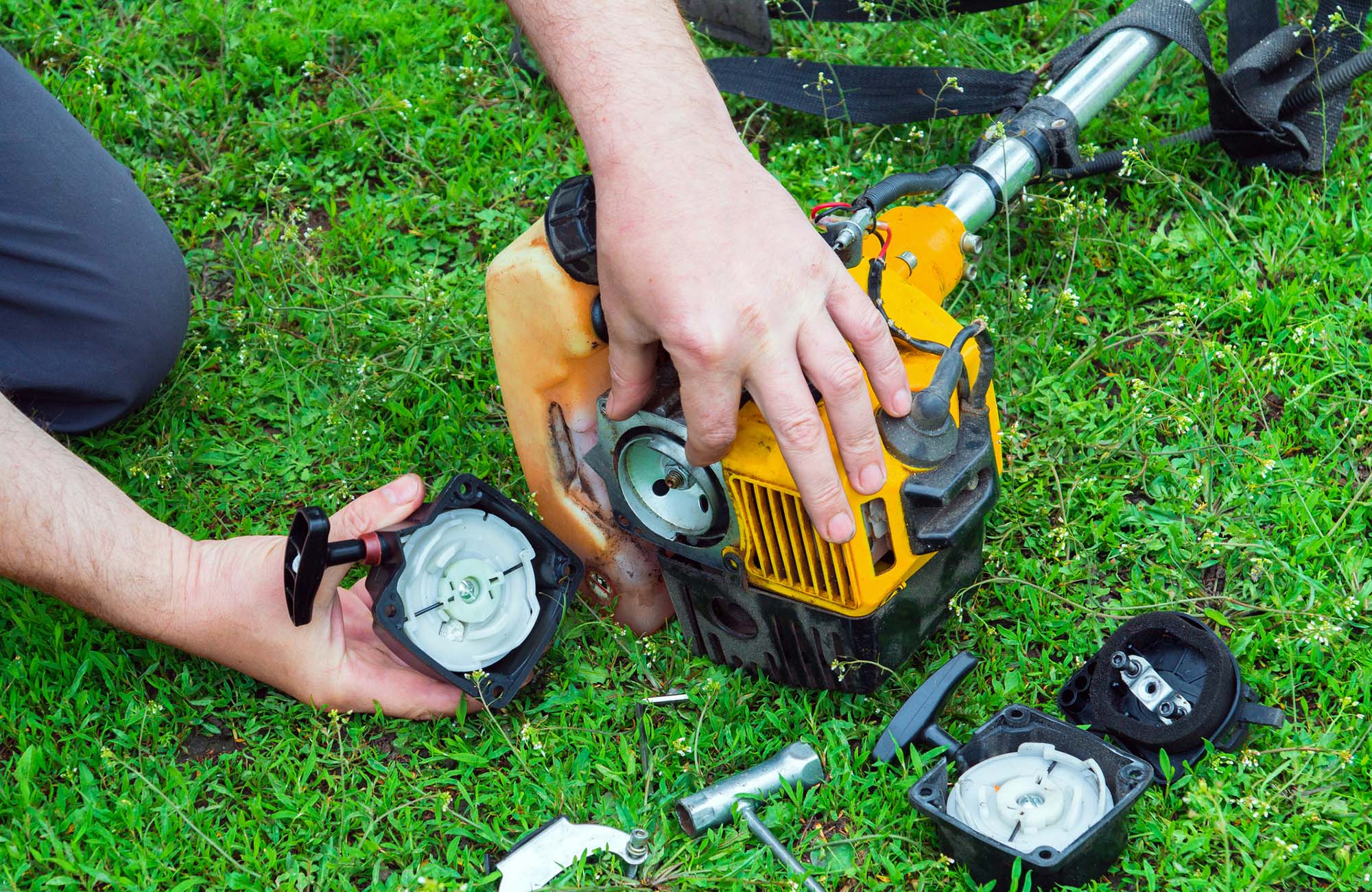 Worker repairs a starter in trimmer or lawn mower that lies on the grass