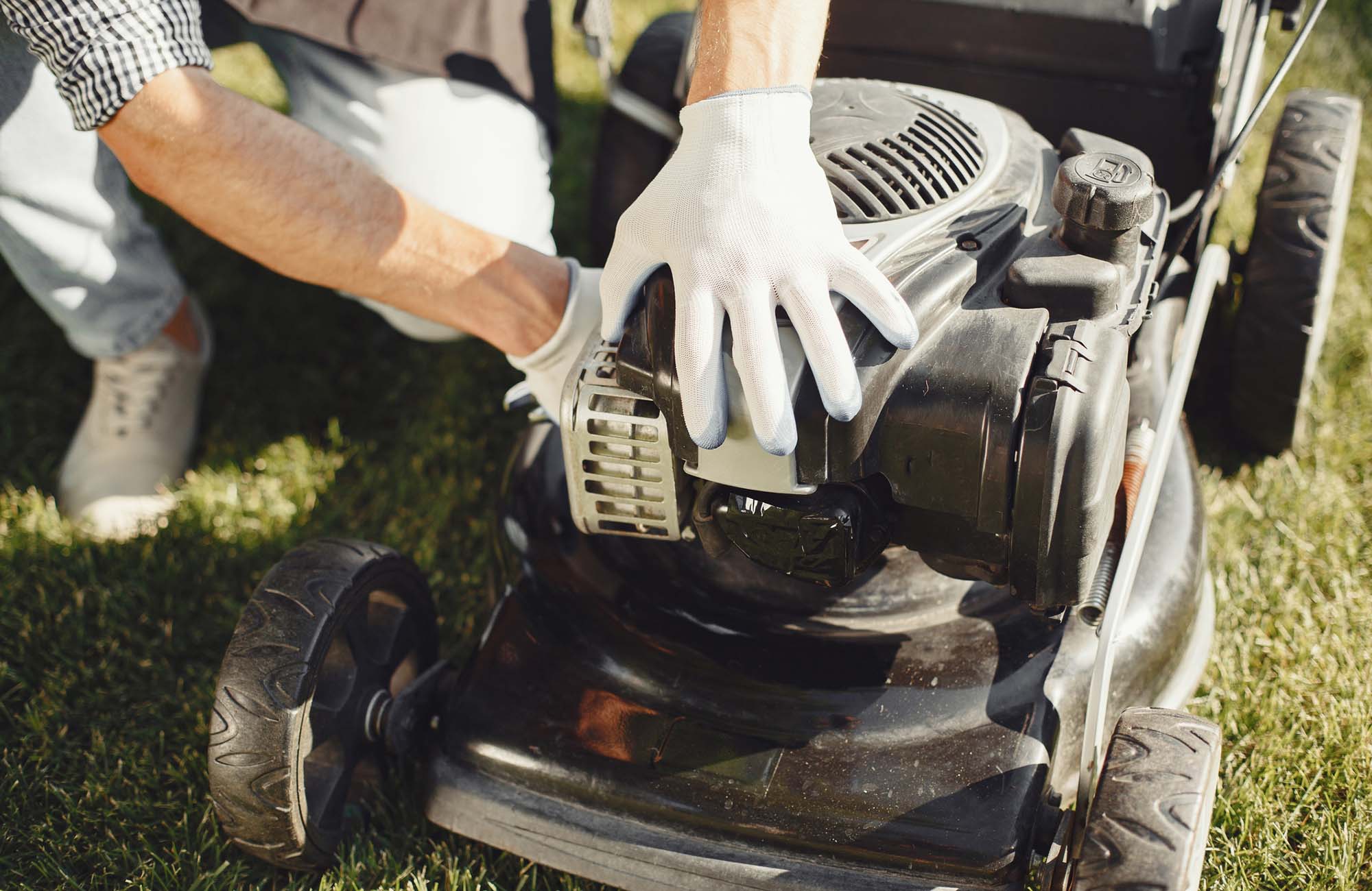 Man cutting grass with lawn mover in the back yard. Male in a black apron. Guy repairs.