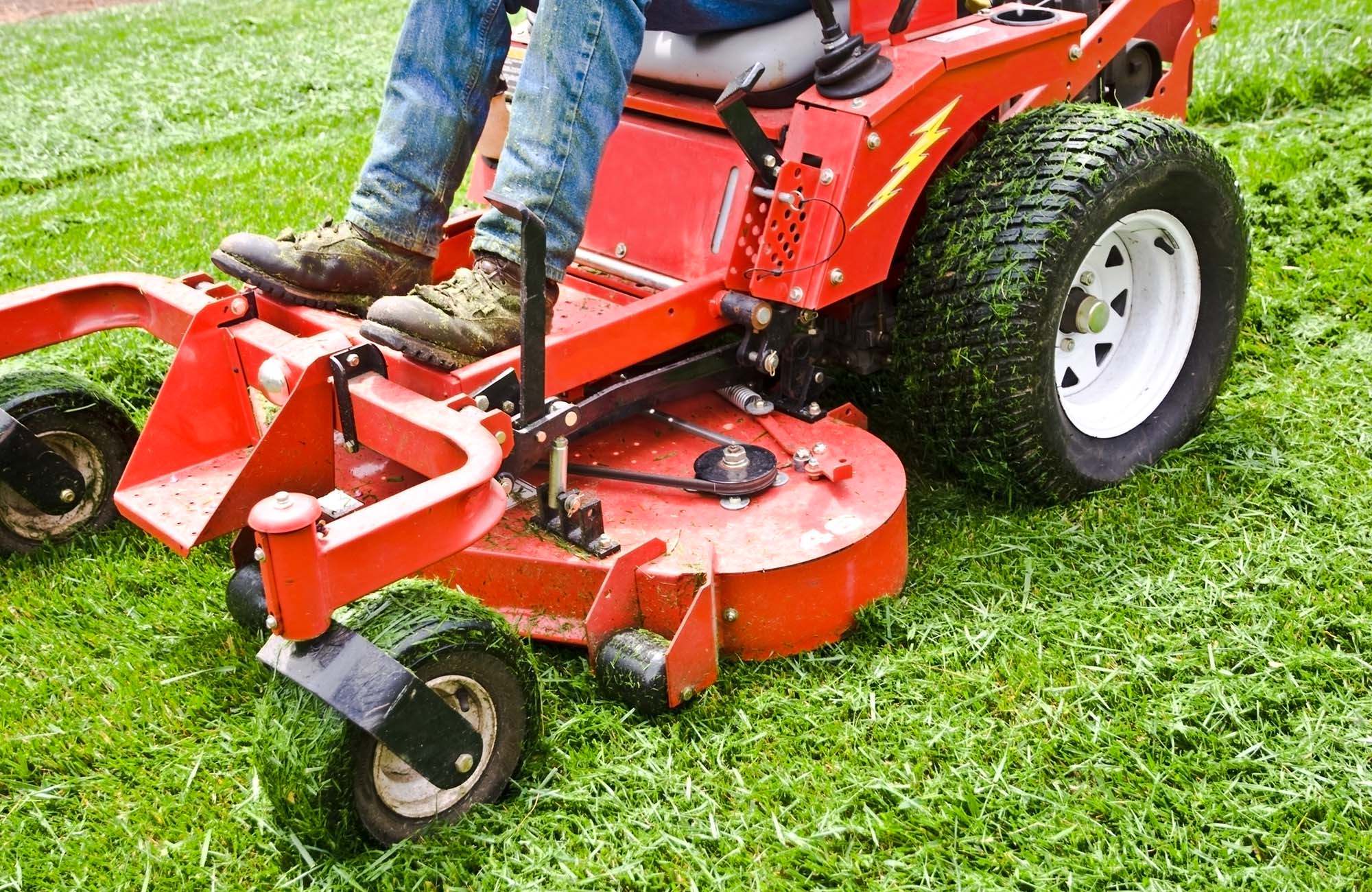 Man on a riding lawn mower that has grass stuck to the wheels. Spring and summer outdoor maintenance.