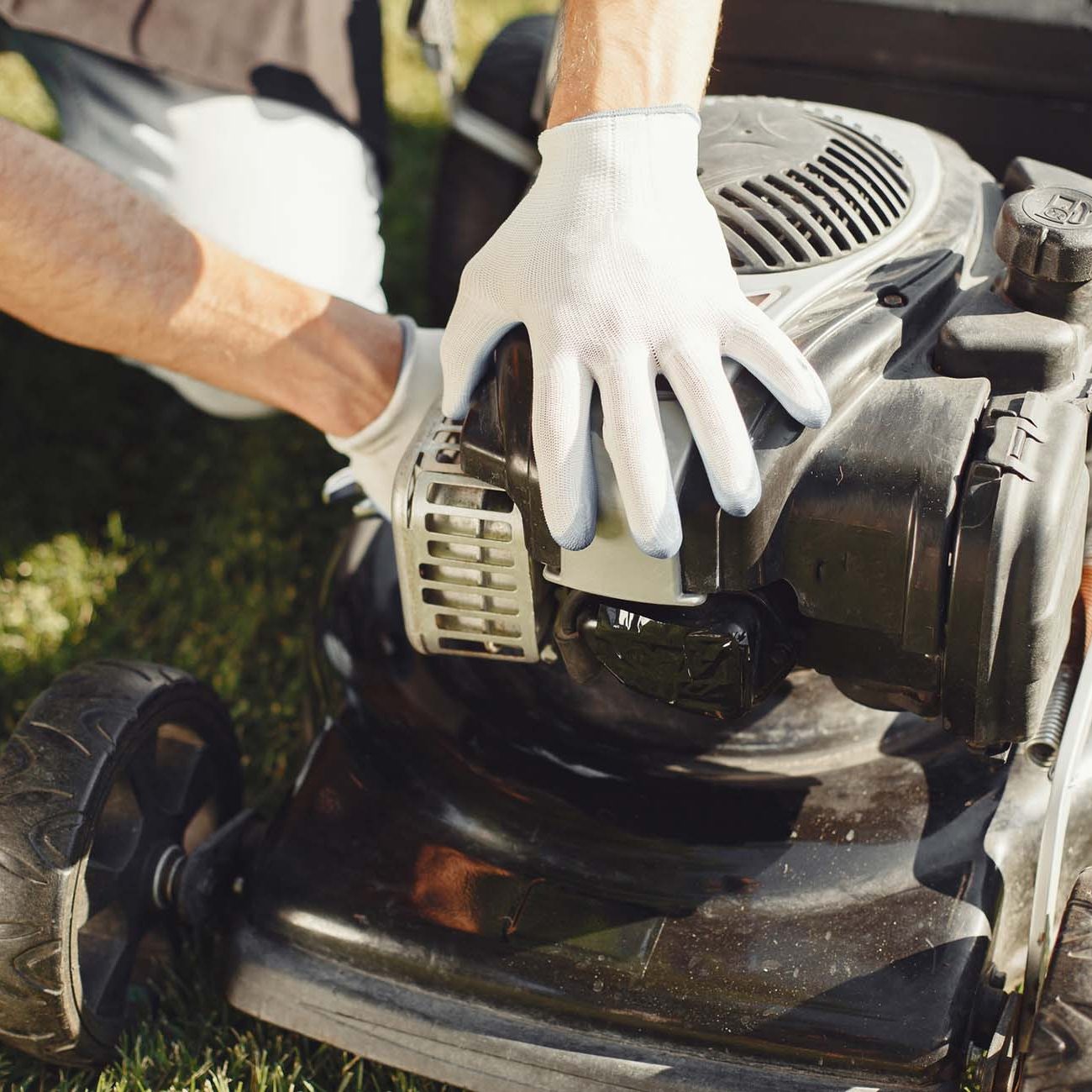 Man cutting grass with lawn mover in the back yard. Male in a black apron. Guy repairs.