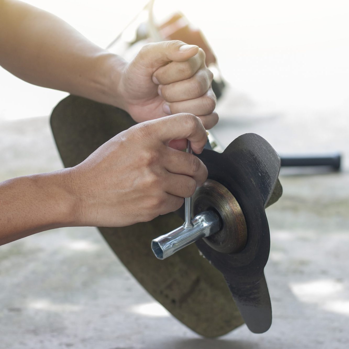 Hand of the mechanic holds the socket wrench to loosen the nut in the lawn mower.